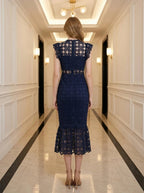 Rear view of a woman in a navy blue lace midi dress with a high neckline and ruffled cap sleeves, standing in a hallway.