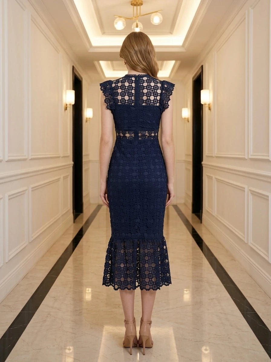 Rear view of a woman in a navy blue lace midi dress with a high neckline and ruffled cap sleeves, standing in a hallway.