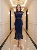 Woman in a navy blue lace midi dress with a high neckline and ruffled cap sleeves, standing in a hallway.