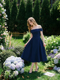 Woman in a navy blue off-the-shoulder dress standing in a garden