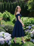 Woman in a navy blue off-the-shoulder dress in a garden setting