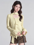woman holding a black purse wearing a light yellow knit top with tie neck