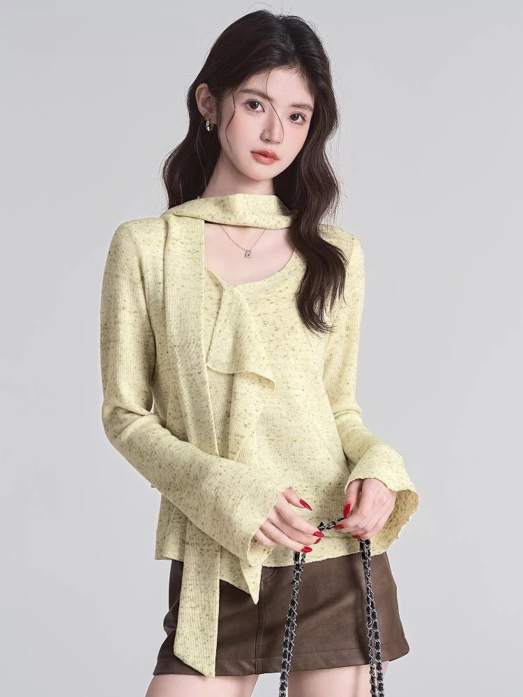 woman holding a black purse wearing a light yellow knit top with tie neck