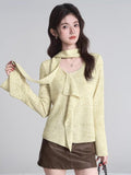 woman wearing a light yellow knit top with tie neck and ruffle detail