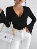 Woman holding a white quilted handbag and wearing a black long-sleeved ribbed knit top with flared sleeves