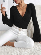 Woman sitting and taking a selfie while wearing a black long-sleeved ribbed knit top with flared sleeves