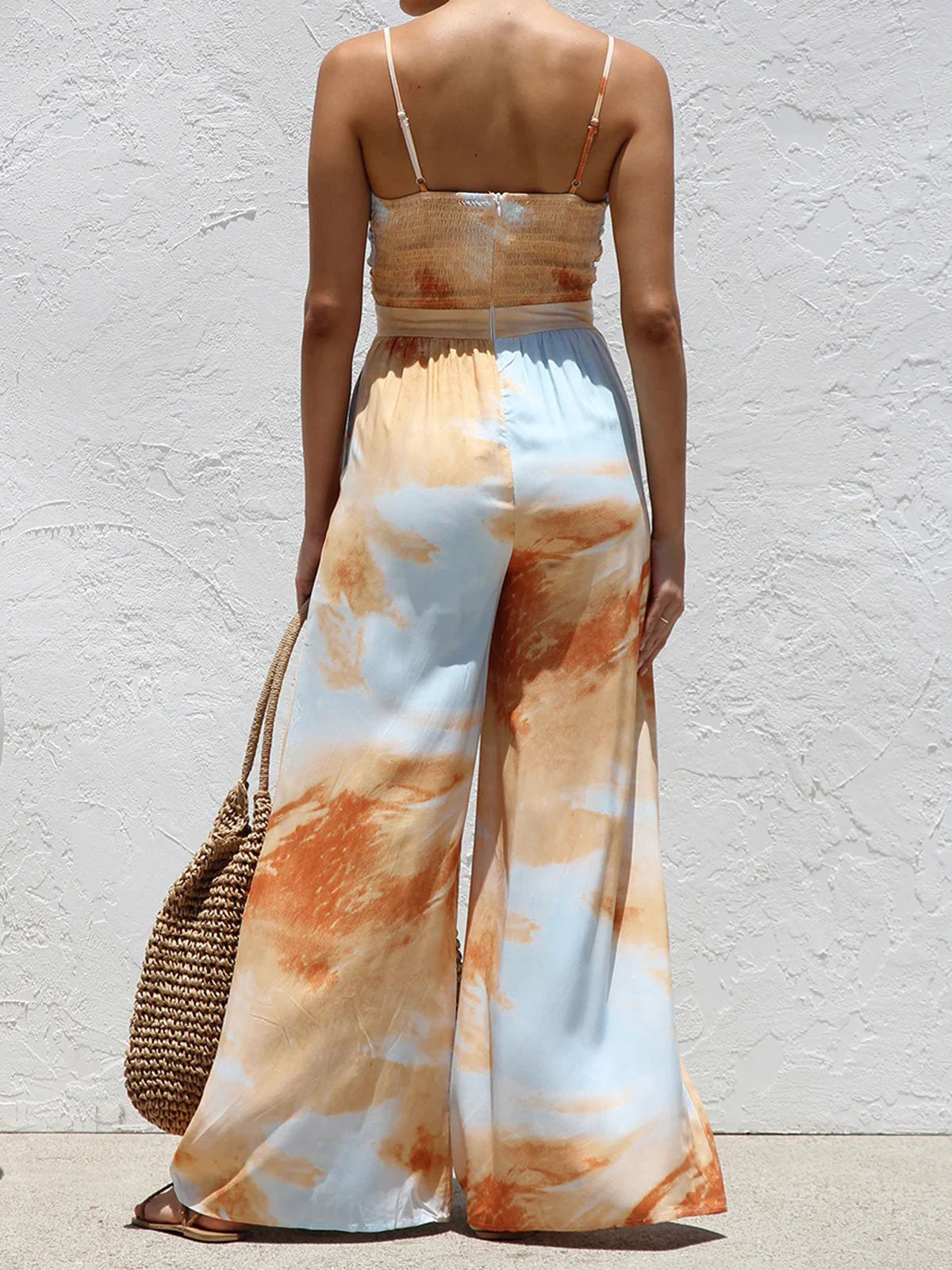 Back view of a woman in a tie-front wide-leg jumpsuit with an abstract print and smocked back.