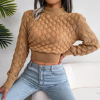 Woman wearing a tan cropped mock neck sweater with textured diamond pattern and light wash jeans.