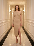 Woman in a beige ribbed knit one-shoulder midi dress with a high slit, standing in a hotel hallway.