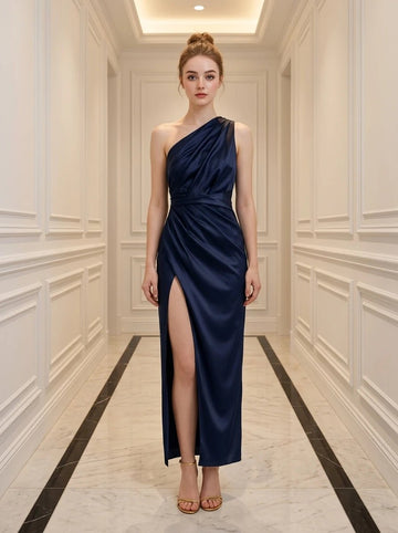 Woman in a navy blue satin one-shoulder gown with a thigh-high slit standing in a hallway.