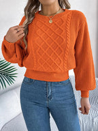 Close-up of a woman's chest and arms in an orange sweater with cable knit detailing.