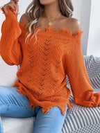 Woman sitting on a couch wearing an orange off-the-shoulder distressed knit sweater
