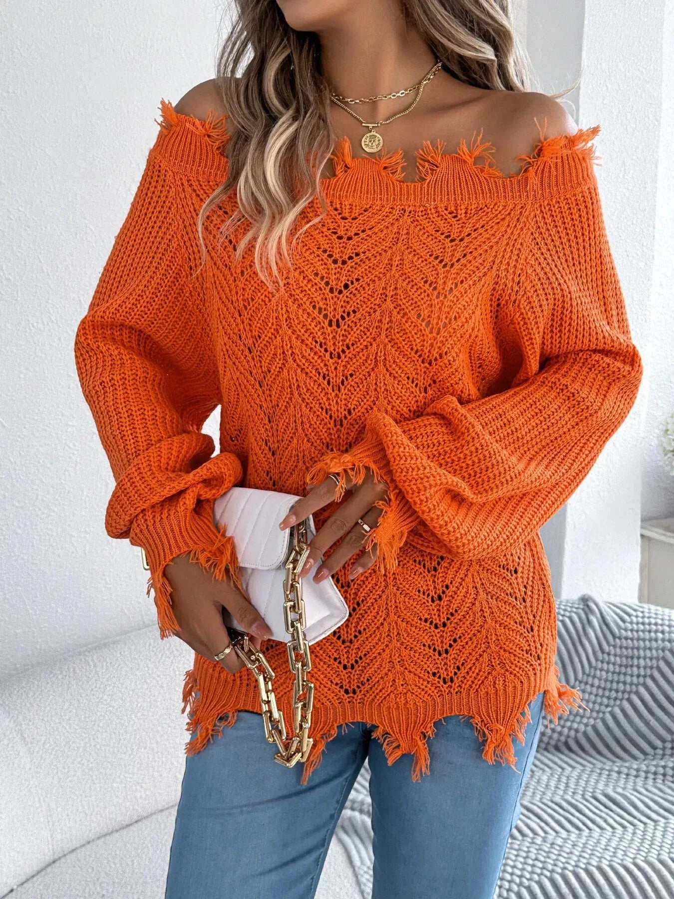 Close-up of a woman wearing an orange off-the-shoulder distressed knit sweater and holding a white clutch