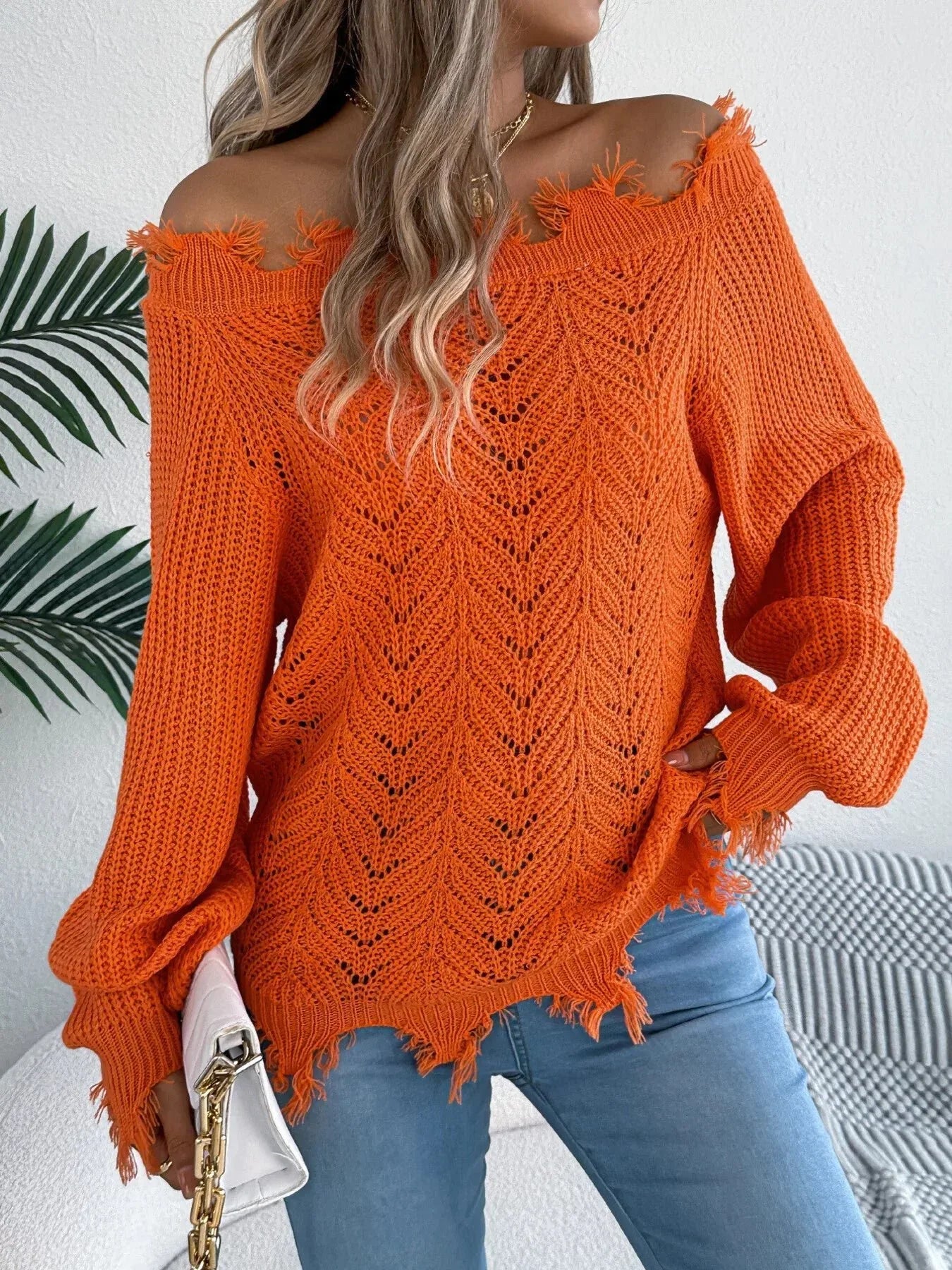 Woman wearing an orange off-the-shoulder distressed knit sweater with light wash jeans Main image