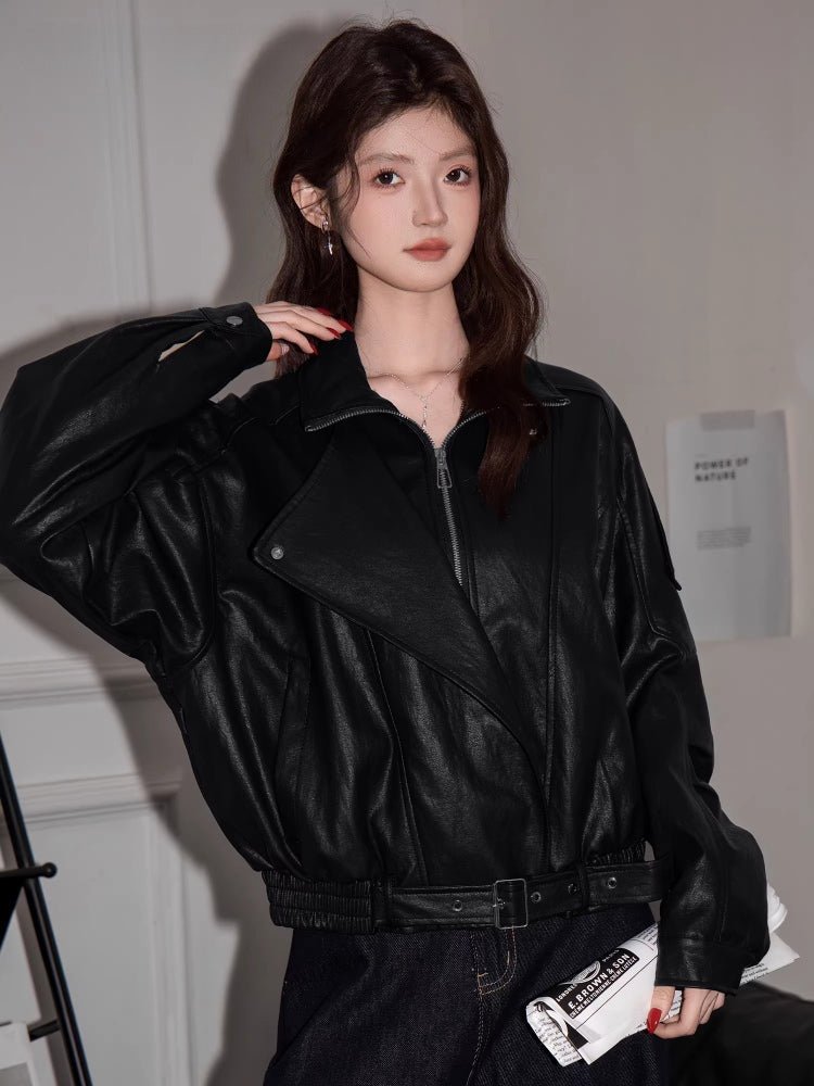 Woman adjusting the collar of a black faux leather bomber jacket with zippered cuffs.