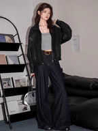 Full body shot of a woman in a black faux leather bomber jacket, grey crop top, and dark wash wide-leg jeans.