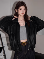 Front view of a woman wearing a black faux leather bomber jacket over a grey crop top.