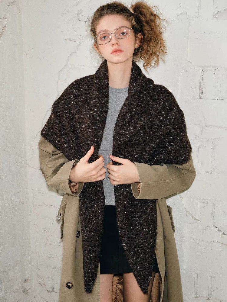 Close-up of a woman wearing a brown textured knit shawl with a white branded detail.