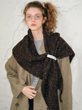 Woman wearing a brown textured knit shawl wrapped around her shoulders over a tan trench coat.