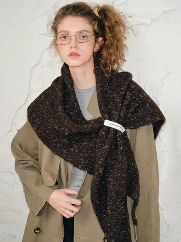 Woman wearing a brown textured knit shawl wrapped around her shoulders over a tan trench coat.