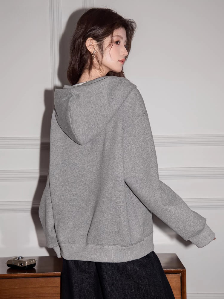 Woman wearing a grey hooded sweatshirt with a v-neck detail and drawstring.