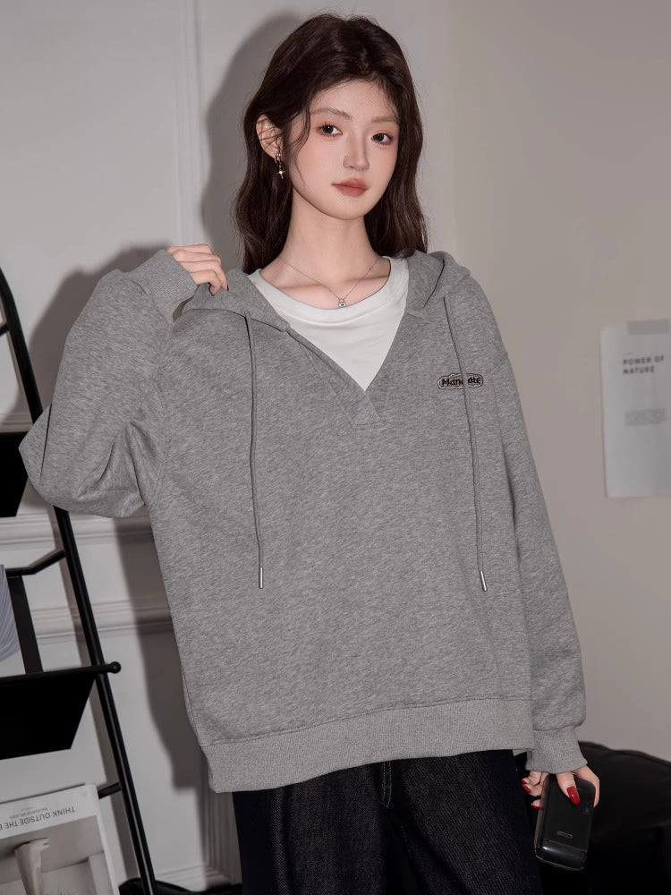Close-up of a woman wearing a grey hooded sweatshirt with a v-neck and drawstring.