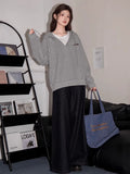 Full body shot of a woman in a grey hooded sweatshirt and dark wide-leg jeans, holding a blue tote bag.