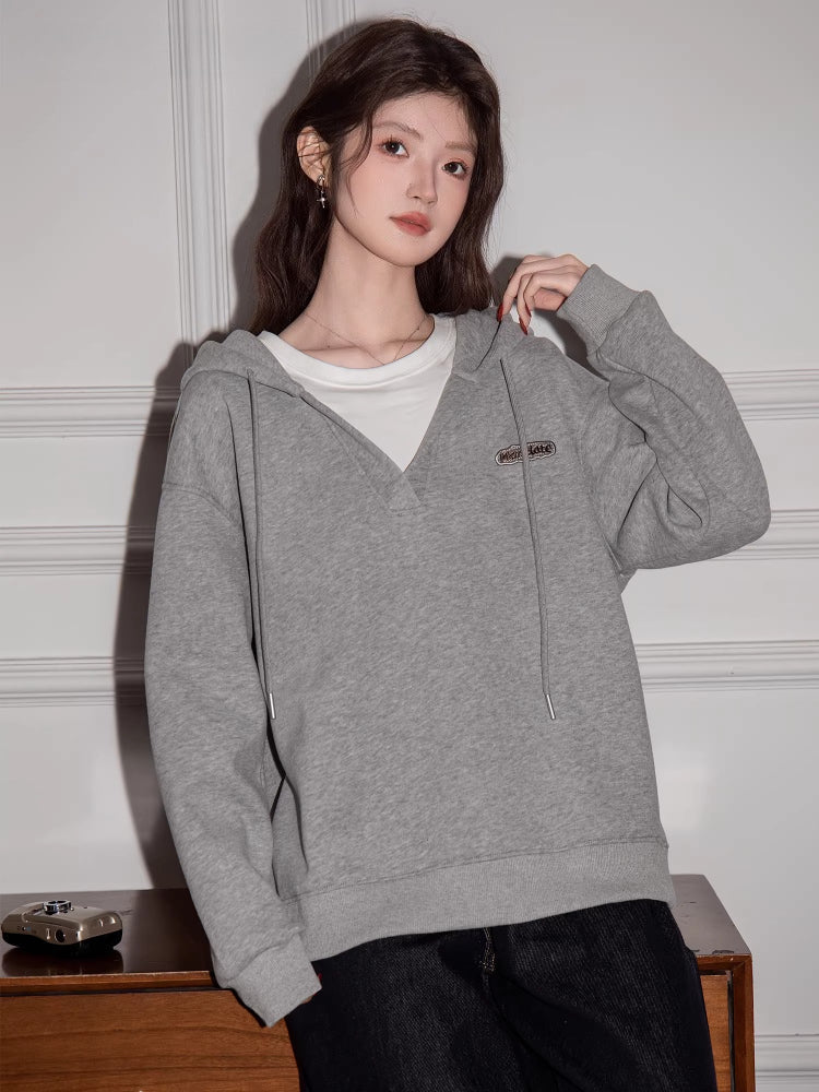 Woman wearing a grey hooded sweatshirt with a v-neck detail and drawstring.