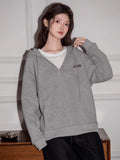 Woman wearing a grey hooded sweatshirt with a v-neck detail and drawstring.