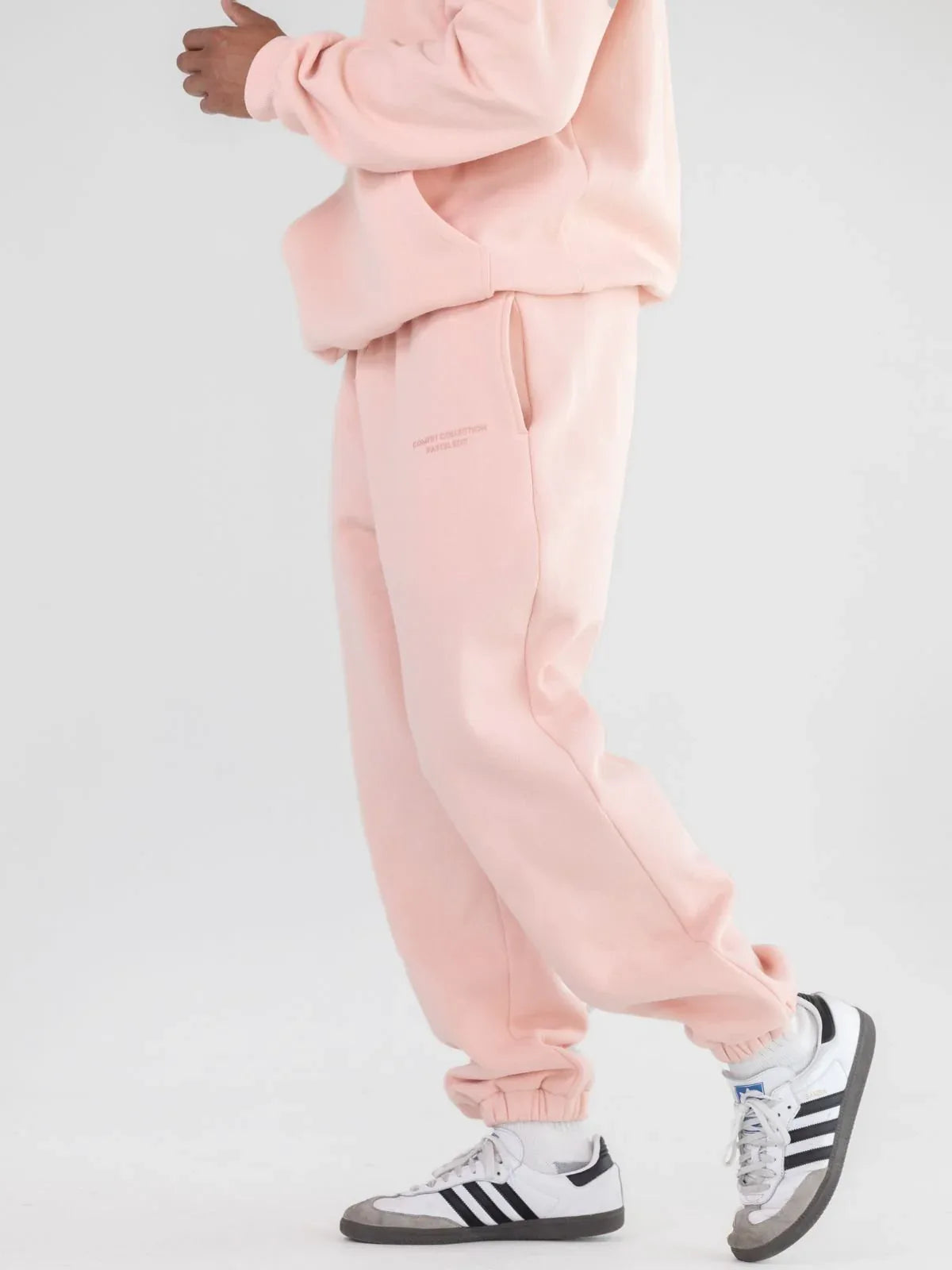 Side view of pink sweatpants with cuffed ankles and sneakers.