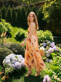 Woman walking in a garden wearing a peach maxi dress with a tropical leaf print.