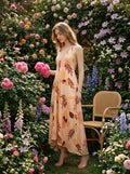 Woman holding a bouquet of pink roses in a garden, wearing a peach maxi dress with a tropical leaf print.