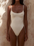 Woman wearing a cream-colored one-piece swimsuit with underwire bust support and gold hardware accents.
