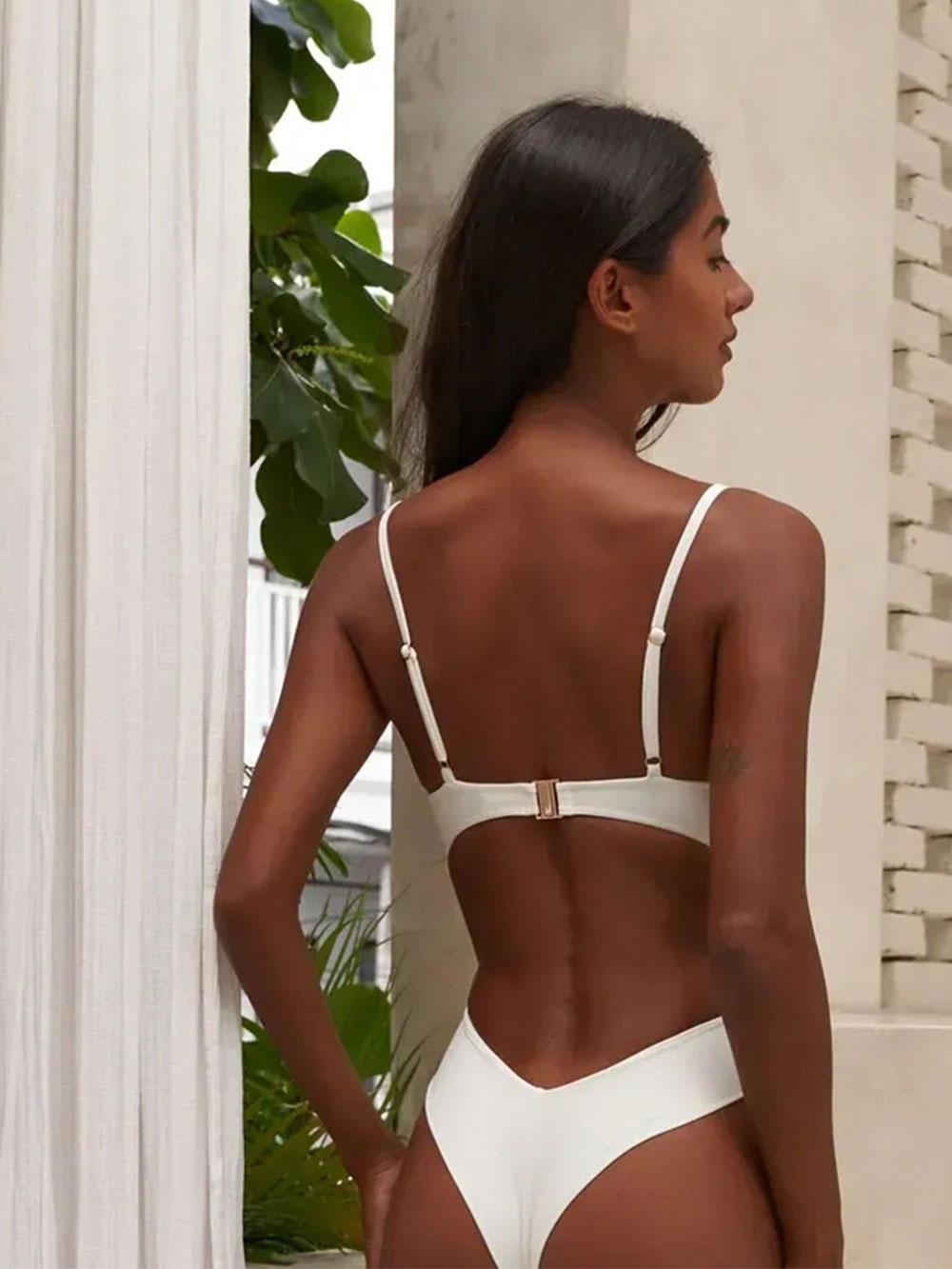 Rear view of a woman wearing a white one-piece swimsuit, showcasing adjustable straps and a high-cut leg.