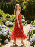 Woman walking in a garden wearing a red floral print midi dress with pleats and cami straps.