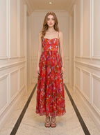 Woman standing in a hallway wearing a red floral print midi dress with pleats and cami straps.