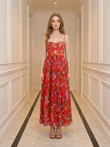 Woman standing in a hallway wearing a red floral print midi dress with pleats and cami straps.