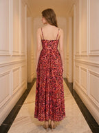 Back view of a woman in a red floral print maxi dress with spaghetti straps and a pleated skirt, standing in a hallway.