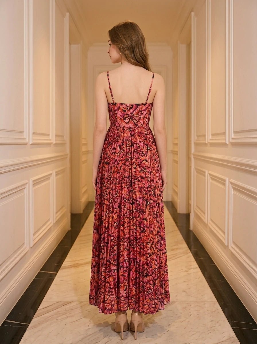 Back view of a woman in a red floral print maxi dress with spaghetti straps and a pleated skirt, standing in a hallway.