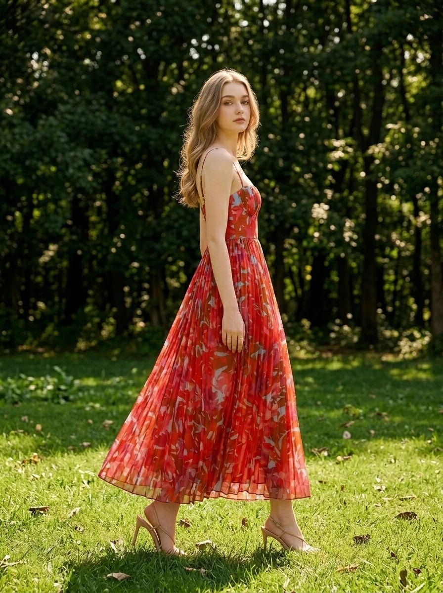 Woman walking in a grassy area wearing a red floral print midi dress with pleats and cami straps.