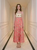 Woman wearing a coral midi dress with a white bodice featuring a bird and floral print, and a skirt with a repeating pattern of small illustrations of birds, cages, and buildings.