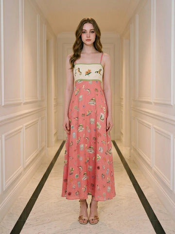 Woman wearing a coral midi dress with a white bodice featuring a bird and floral print, and a skirt with a repeating pattern of small illustrations of birds, cages, and buildings.