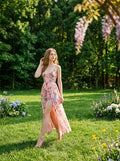 Woman looking away while wearing a pink floral print maxi dress with a thigh-high slit in a park.