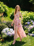 Woman walking in a pink floral print maxi dress with a thigh-high slit in a garden.