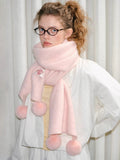 A woman styled with a cozy pink knit scarf featuring decorative pom-poms.