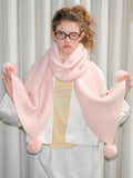 Woman posing with a pastel pink scarf adorned with soft pom-poms.