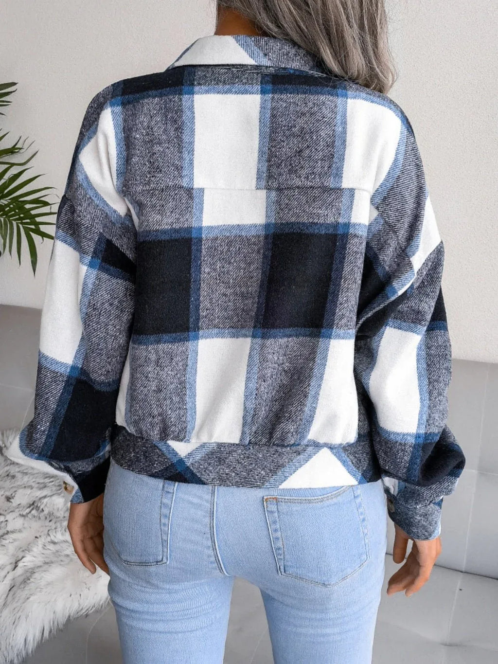 Back view of a woman wearing a blue, black, and white plaid flannel shirt jacket.
