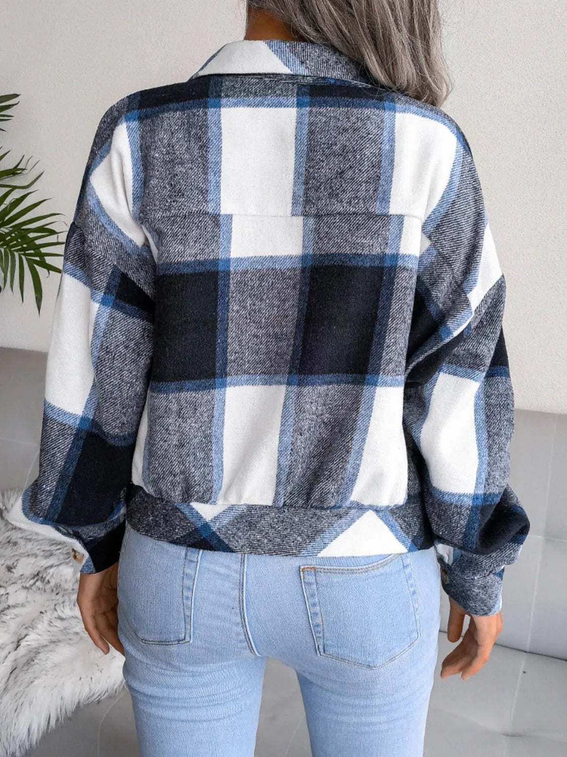 Back view of a woman wearing a blue, black, and white plaid flannel shirt jacket.