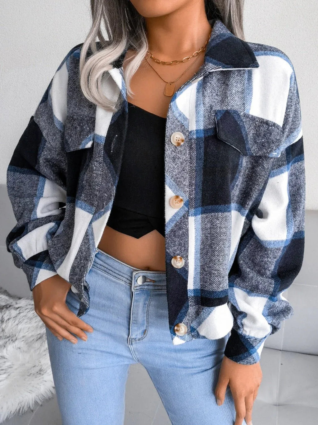 Woman wearing a blue, black, and white plaid flannel shirt jacket with a black crop top and light wash jeans.