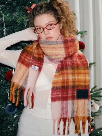 Model wearing a red, orange, and yellow plaid scarf with fringe details.